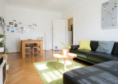 Wohnungsfoto - Wohnzimmer Blick Richtung Türe. Man sieht den Esstisch, das Sofa und weitere Einrichtungsgegenstände im Wohnzimmer.